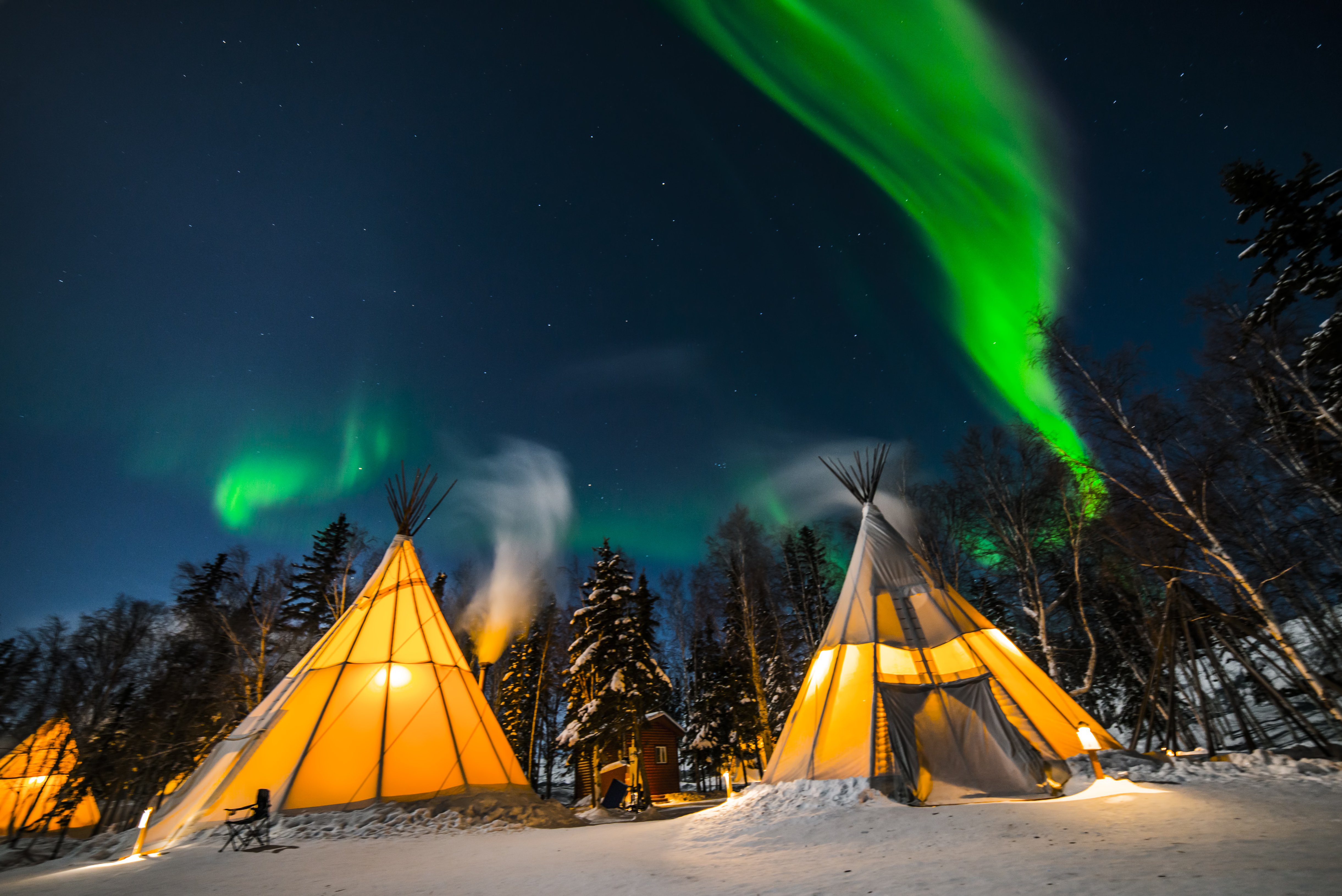 Aurora Village teepees with green aurora in the night sky in Yellowknife, NT. 